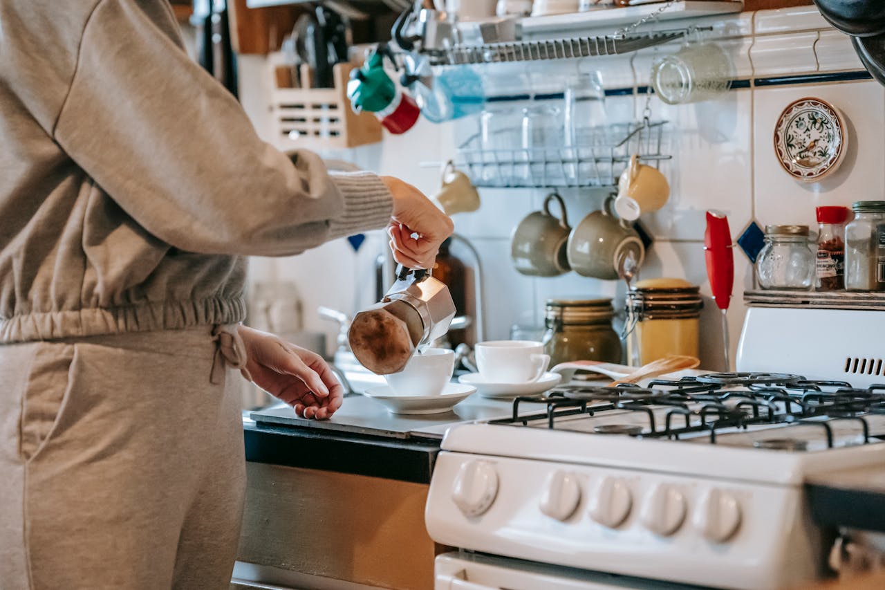 A woman in a cozy kitchen prepares a cup of coffee using a moka pot on a gas stove.